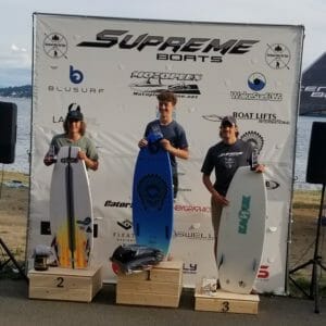 Three surfers on a podium with surfboards in front of them.