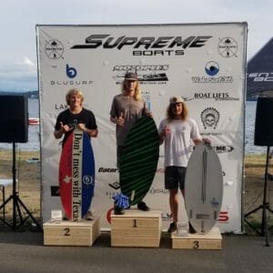 Three surfers standing on podiums next to water with Supreme Boats.