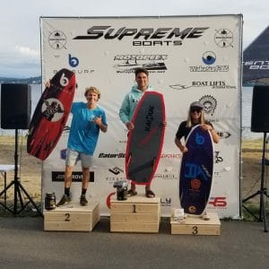 Three people standing on a podium with surfboards at the Supreme Boats event.