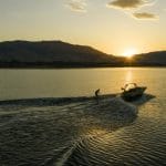A man is riding a Supreme boat on a lake at sunset.