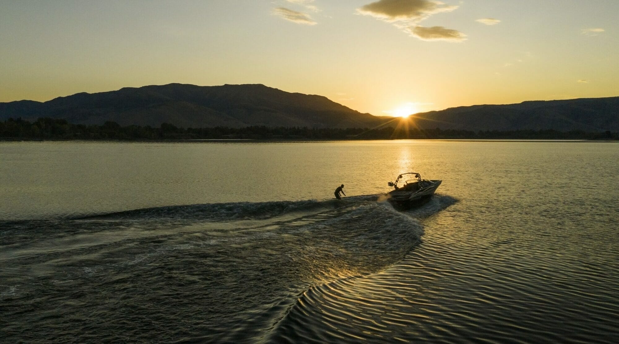 A man is riding a Supreme boat on a lake at sunset.