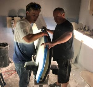 Two men working on a Supreme surfboard in a room.