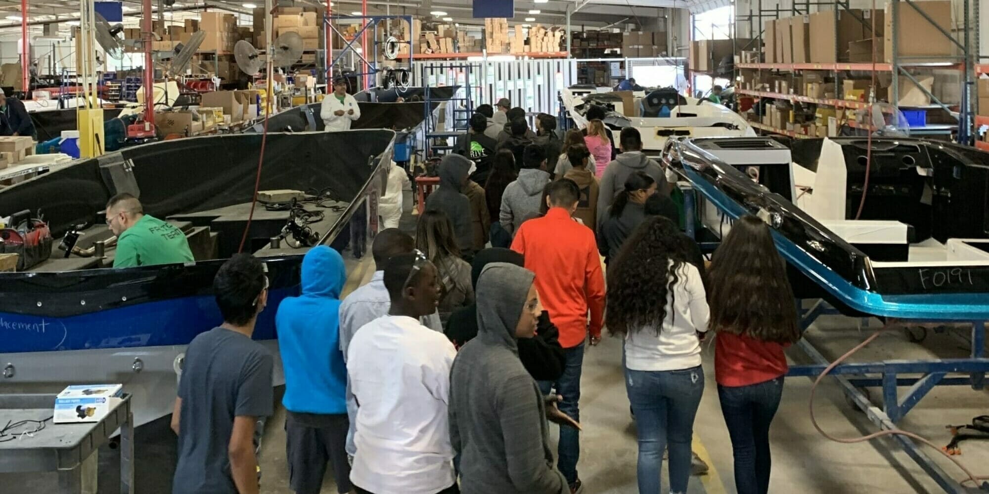 A group of people standing in a warehouse looking at Supreme Boats.