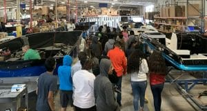 A group of people standing in a warehouse looking at Supreme Boats.