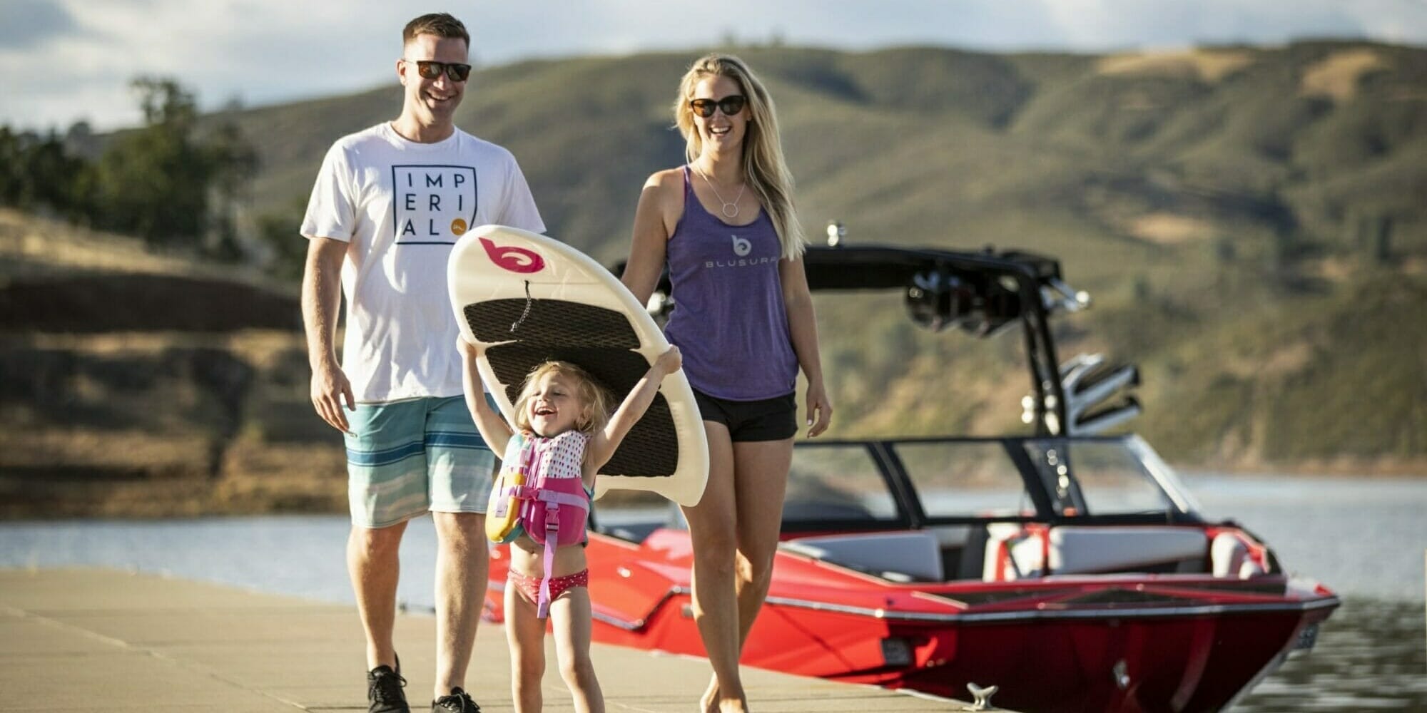 A family with a boat and a surfboard walks down a dock.
