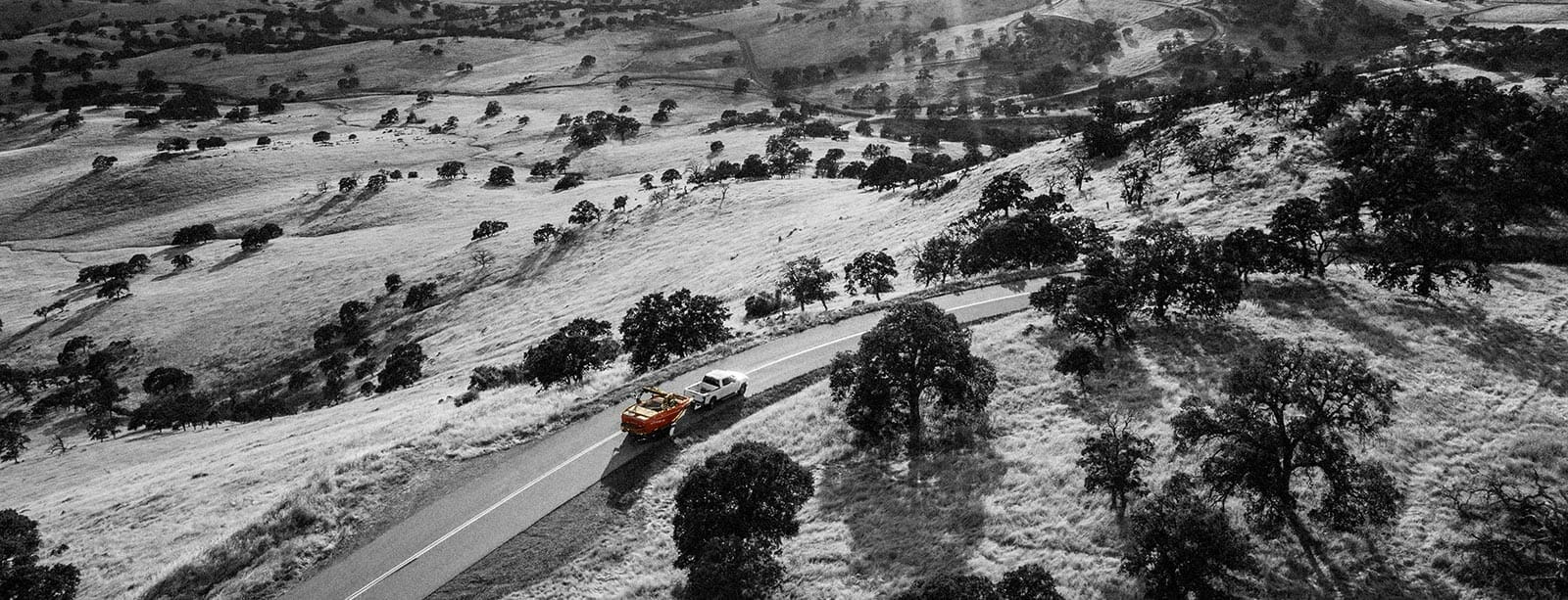 A black and white photo of a car driving down a hill.