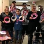 A group of people posing for a photo while making Valentine wreaths.