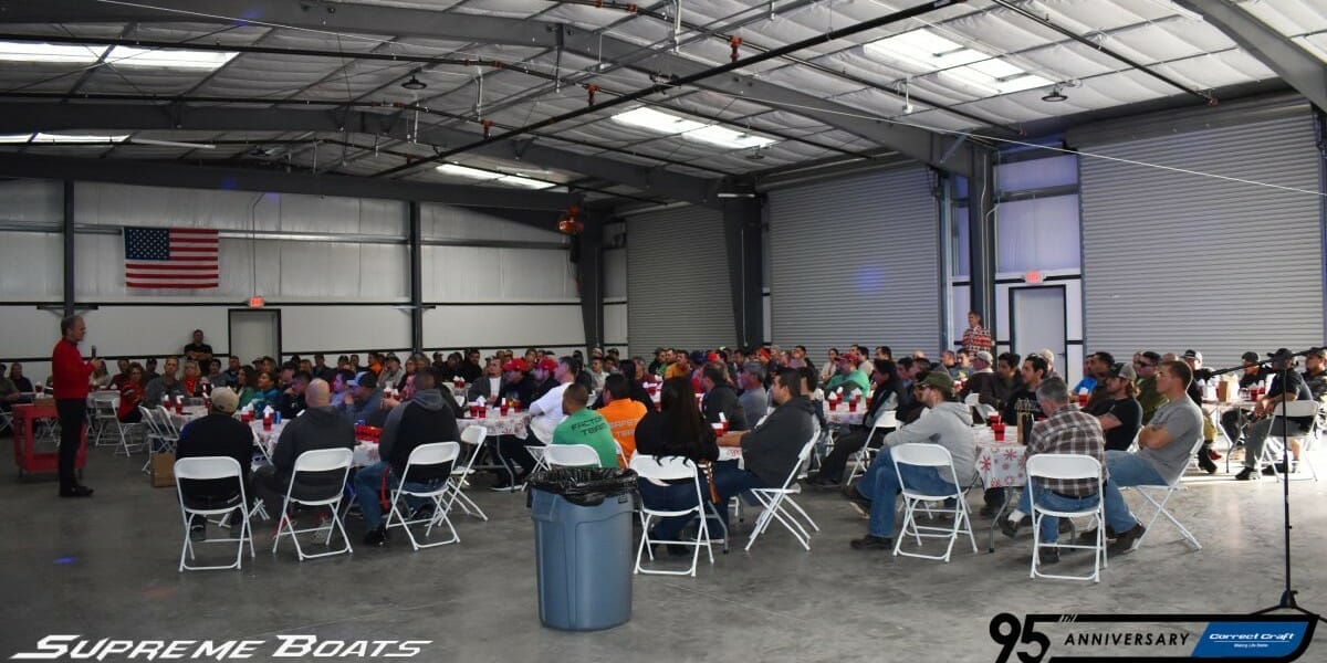 A large group of people sitting at tables in a warehouse showcasing Supreme Boats.