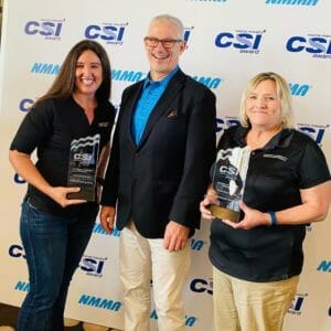 Three people standing in front of a Supreme wall with CSI awards.