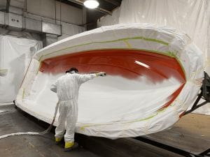 A man in a supreme white suit painting a boat.