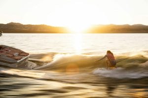 A woman is riding a surfboard on a Supreme boat at sunset.