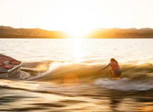 Woman surfing behind boat at sunset