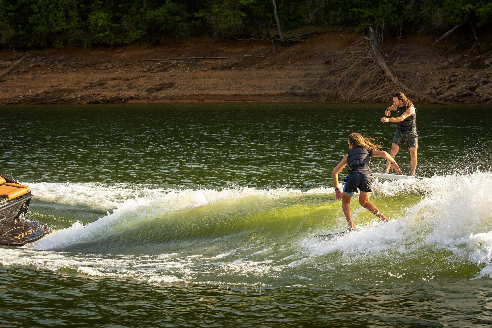 Two people riding Supreme surfboards on a boat.