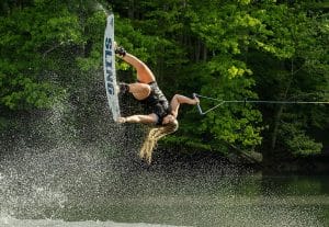 A woman is performing a wakeboarding trick behind a Supreme boat.