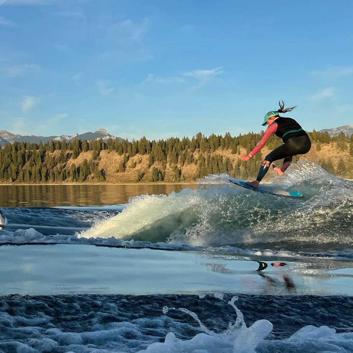 A person riding a surfboard on a lake with a Supreme Boat.