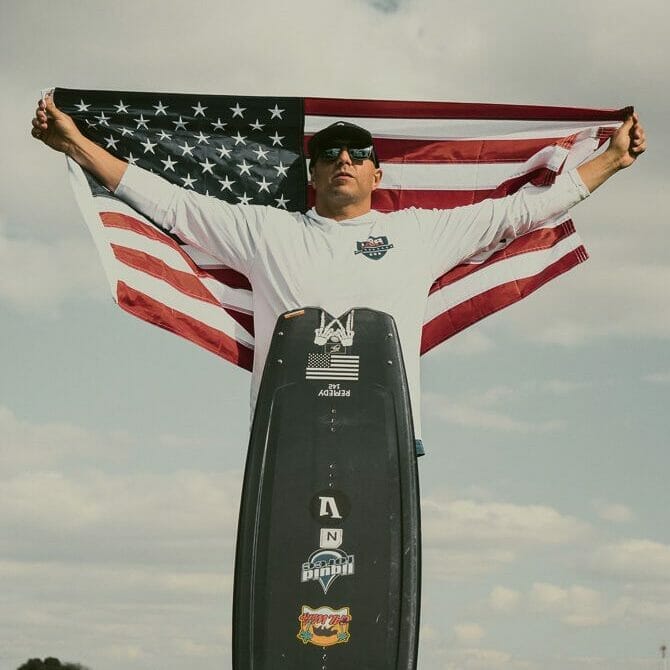 A man holding an American flag atop a Supreme surfboard.