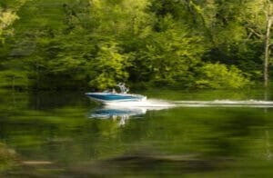 A person is driving a Supreme boat on a lake in a wooded area.