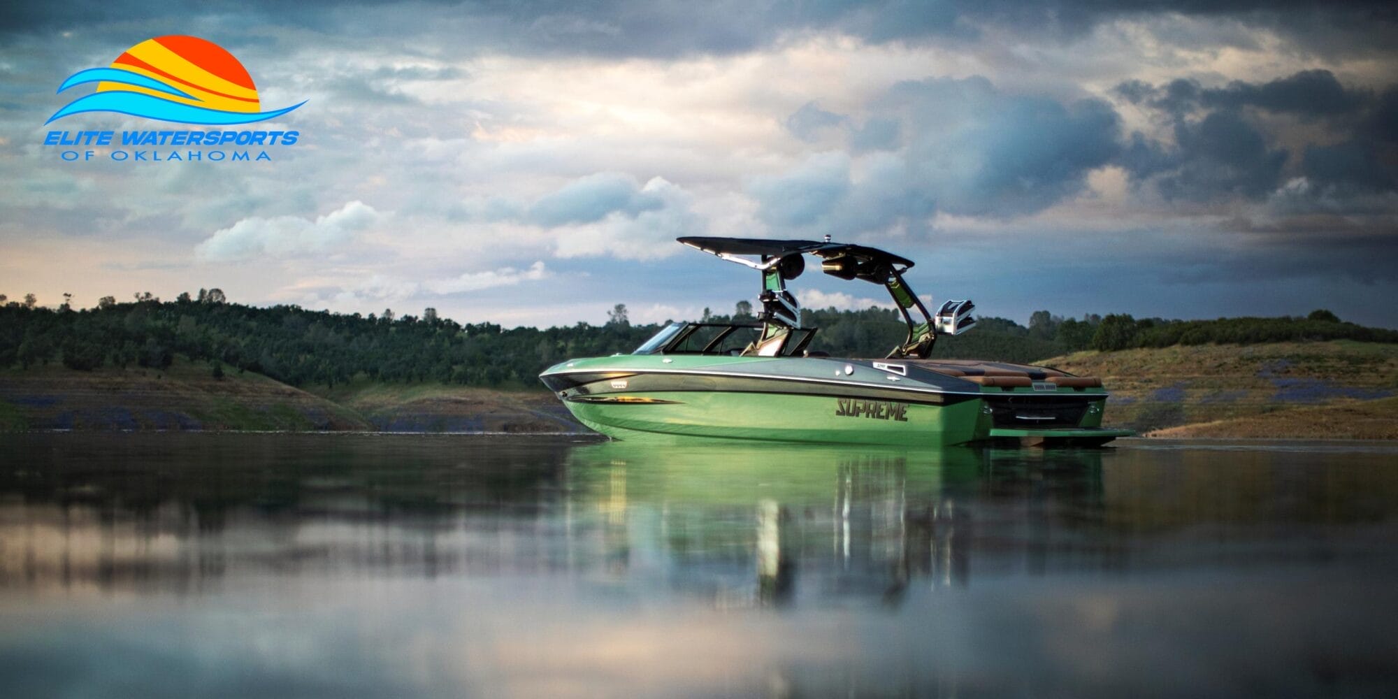 A Supreme-branded boat floats on a calm lake with hilly terrain in the background, showcasing the quality synonymous with Centurion. The Elite Watersports of Oklahoma logo is prominently displayed in the upper left corner.